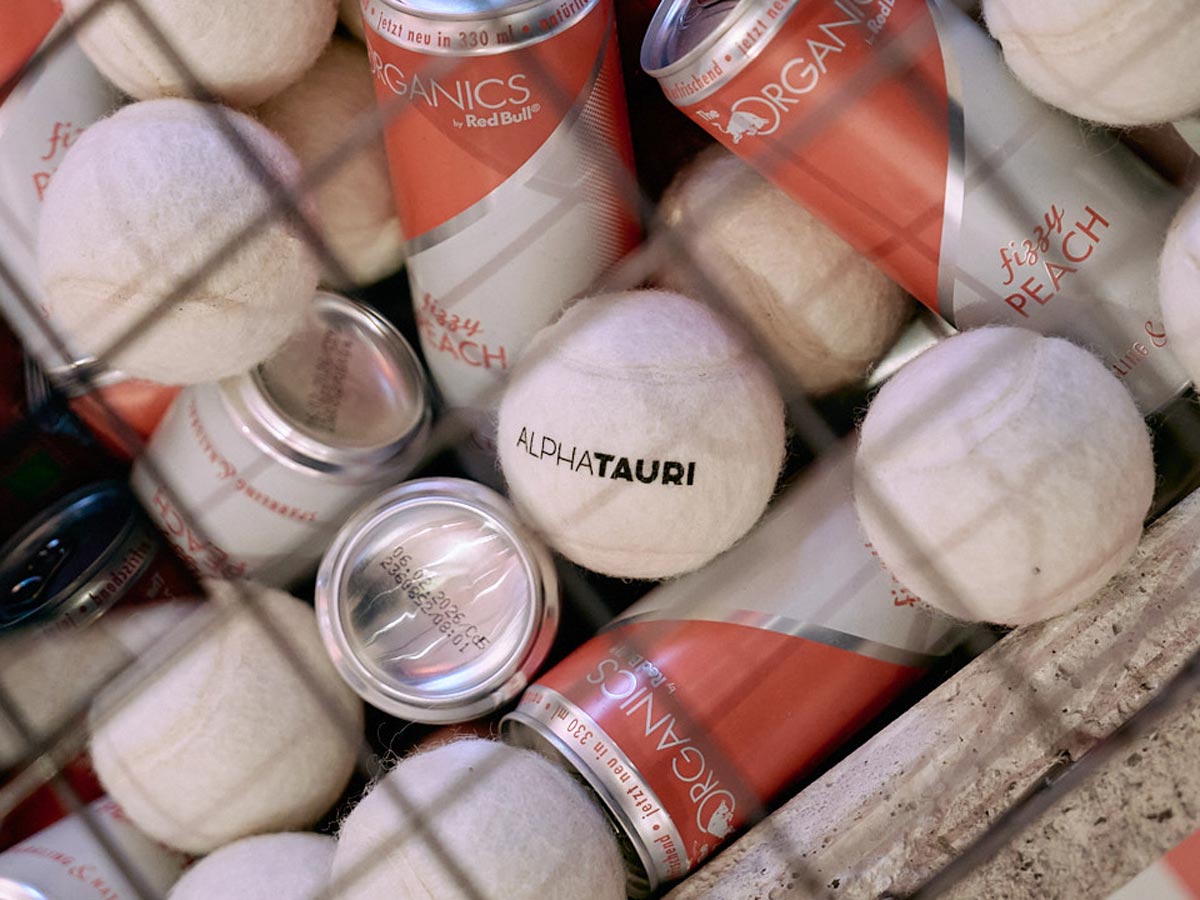 Tennisball mit Schriftzug umrundet von Energy-Dosen und anderen Tennisbällen