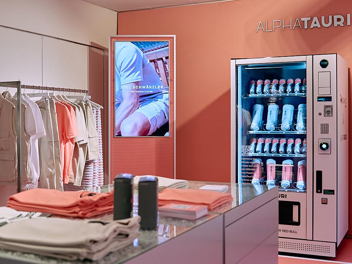Laden mit Kleidung, einem Bildschirm mit Werbung und einem Schriftzug über einem Getränkeautomaten