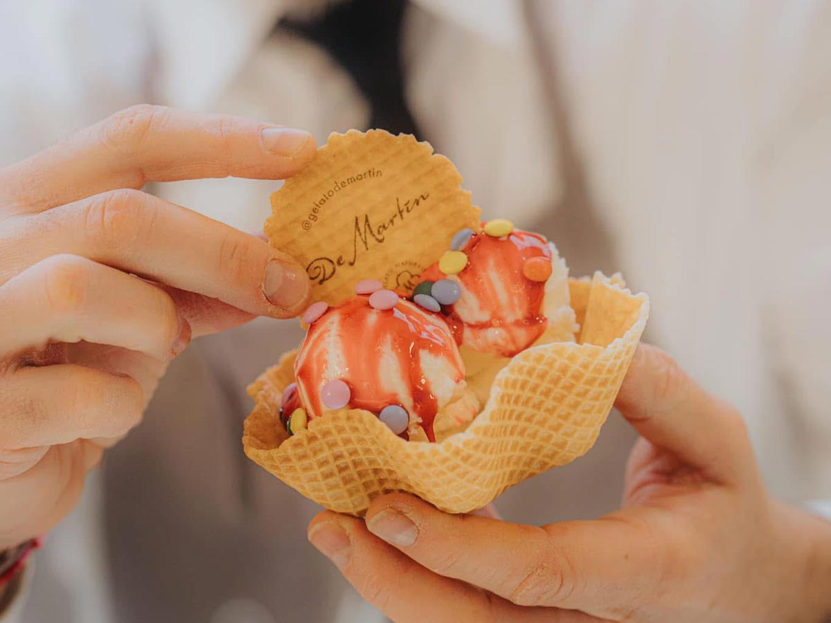 Mann hält zwei Eiskugeln in einem Waffelbecher in die Kamera