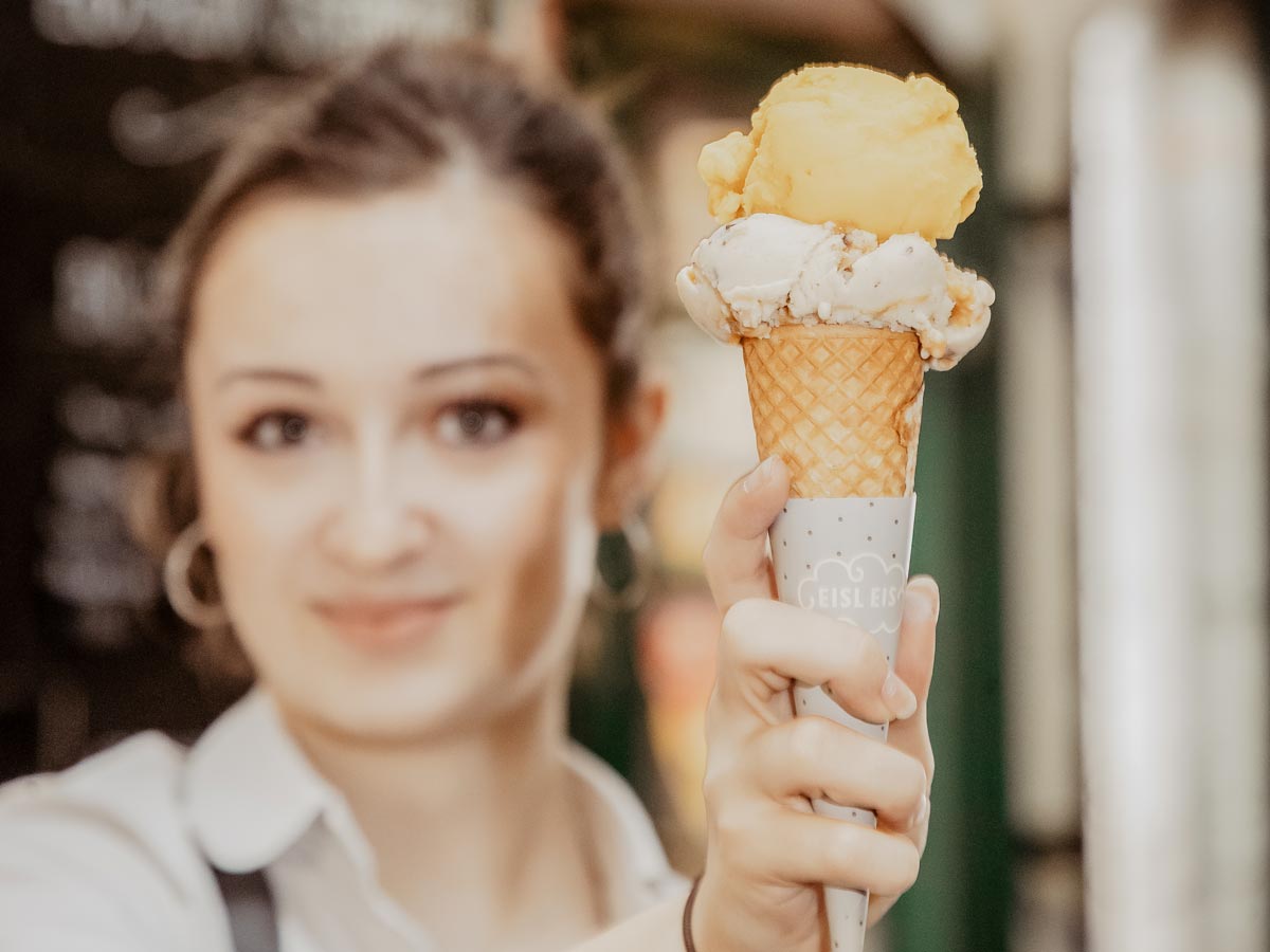 Frau hält zwei Eiskugeln auf einer Waffel in die Kamera