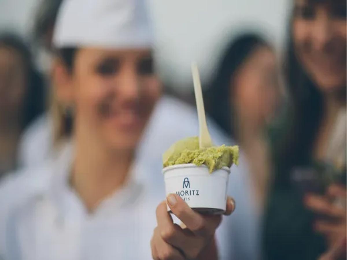 Frau hält eine grüne Eiskugel in einem Becher vor die Kamera